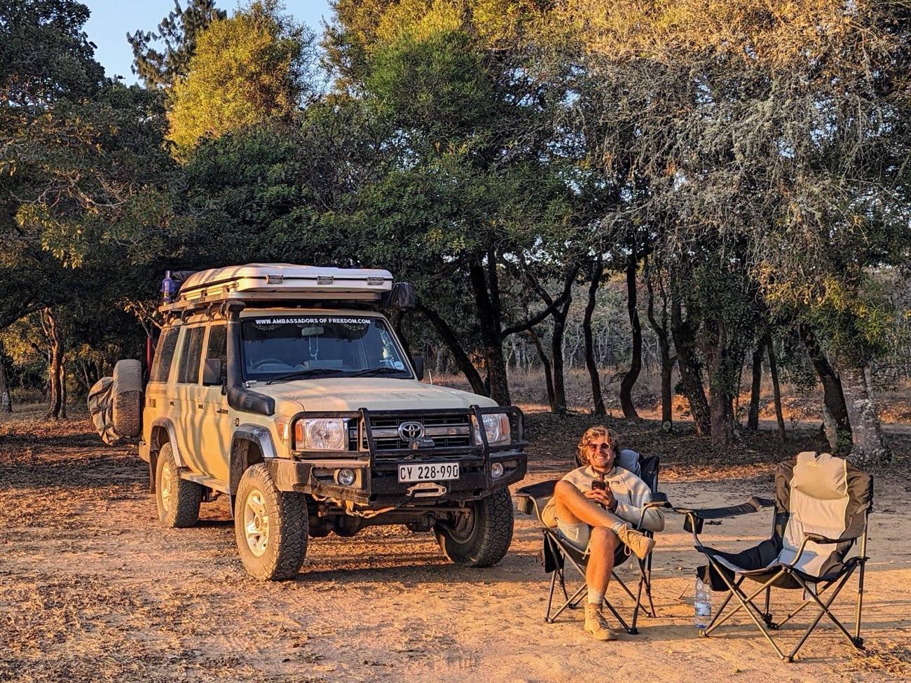 Visit Africa Publishers op een bush kampeerplek bij zonsondergang, kampingstoelen en Land Cruiser naast hem