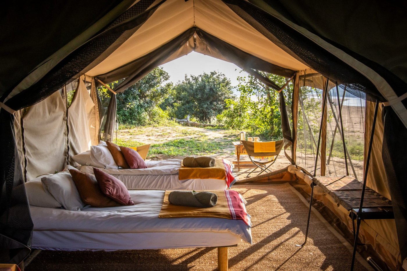 Twee bedden met kussens kijken uit op open canvas deuren bij Chilojo Bush Camp.