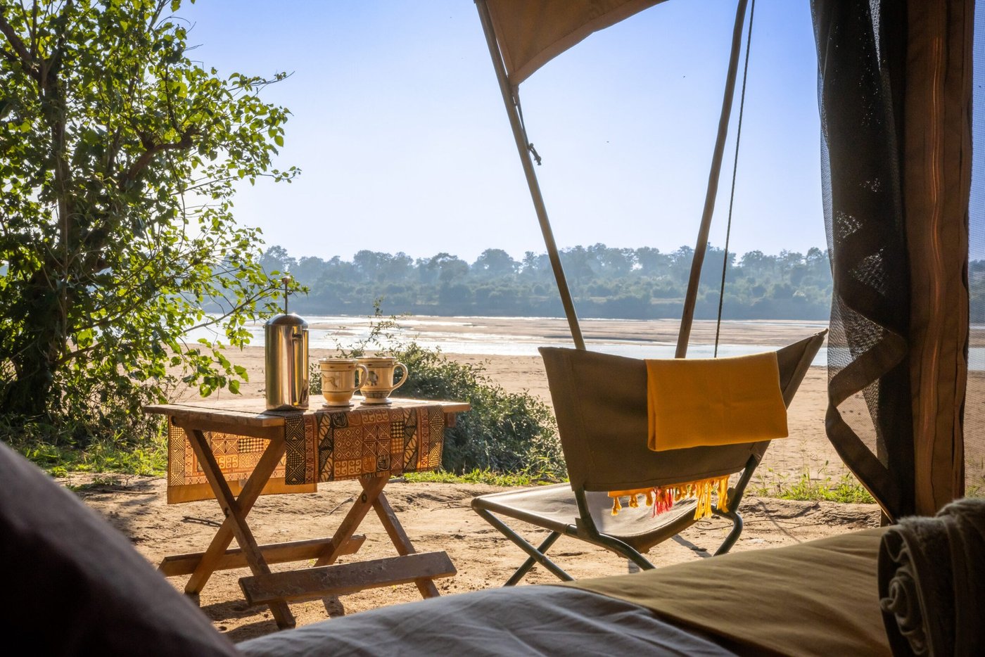 Een tafel en stoelen kijken uit op het droge rivierbedding vanuit het terras van Chilojo Bush Camp.