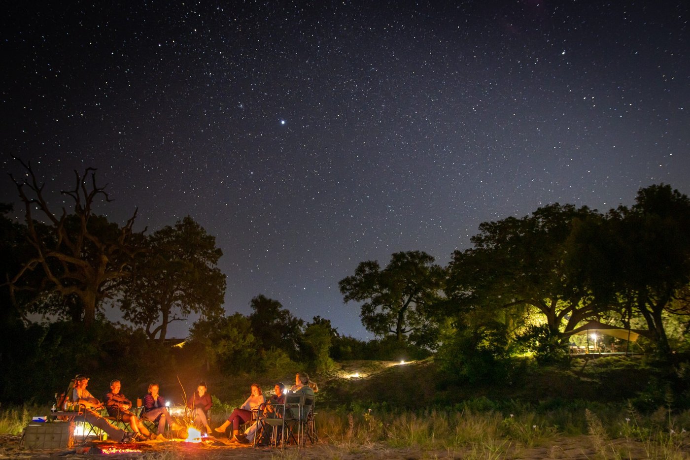 Gasten verzamelen zich bij vuurlicht onder een sterrenhemel bij Chilojo Bush Camp.