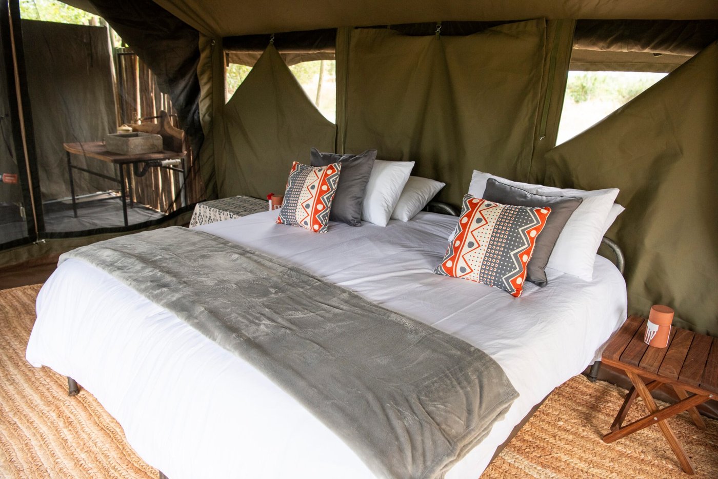 Een gedessineerde plaid en kussens versieren het bed in een Mahove Bush Camp tent.