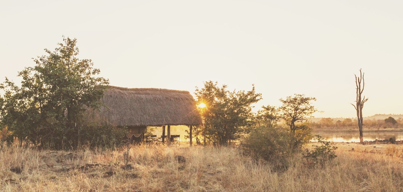 Een rieten dak vangt de zonsondergang over een Gonarezhou-pan op bij Mananga Camps.