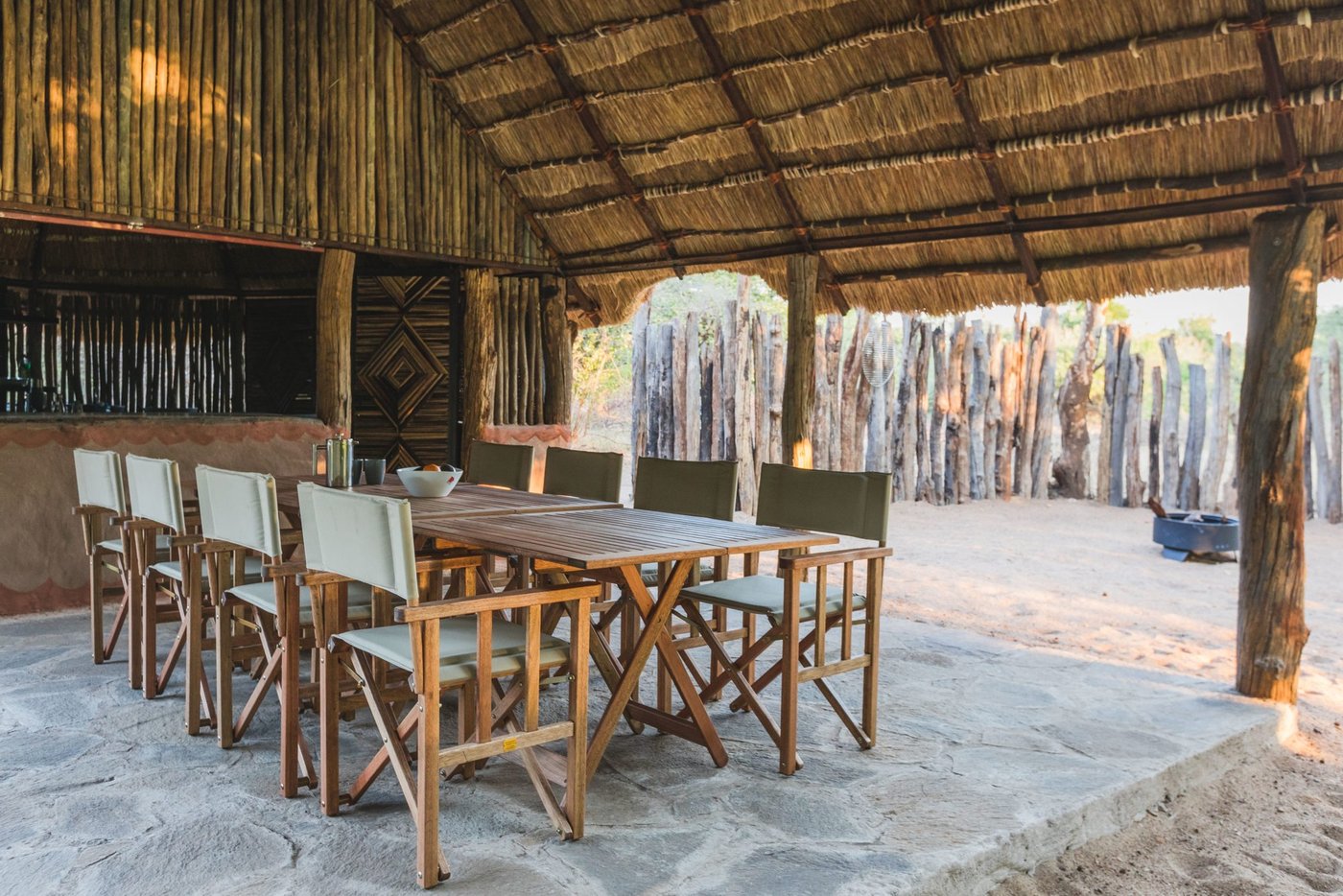 Houten stoelen langs een lange tafel onder riet bij Mananga Camps.